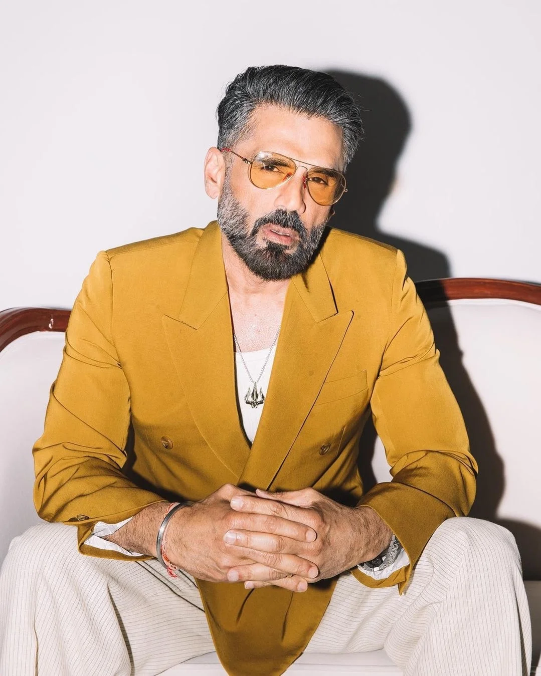 Sunil Shetty seated confidently in a stylish mustard blazer and sunglasses.
