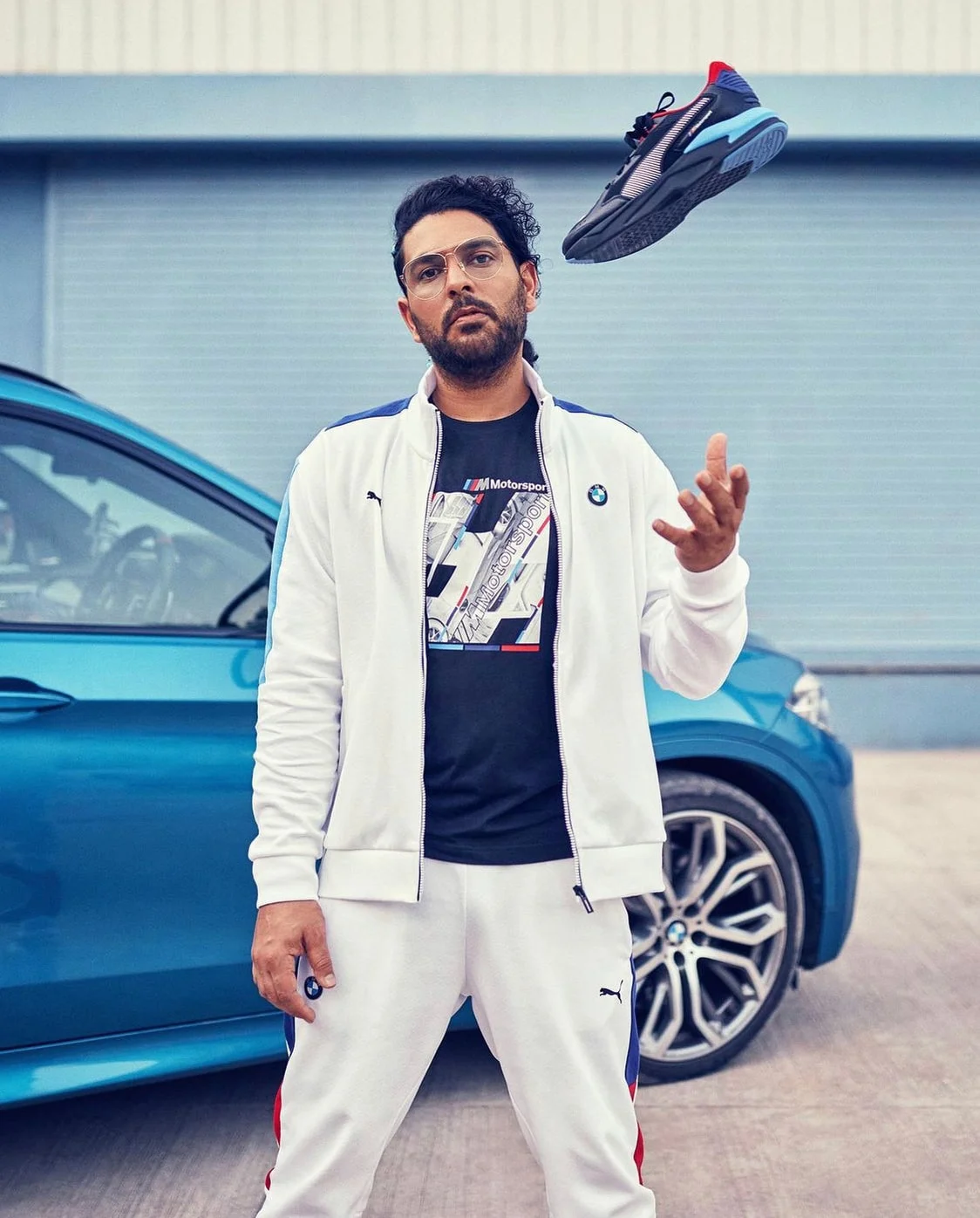 Yuvraj juggling a sneaker in front of a blue BMW car.