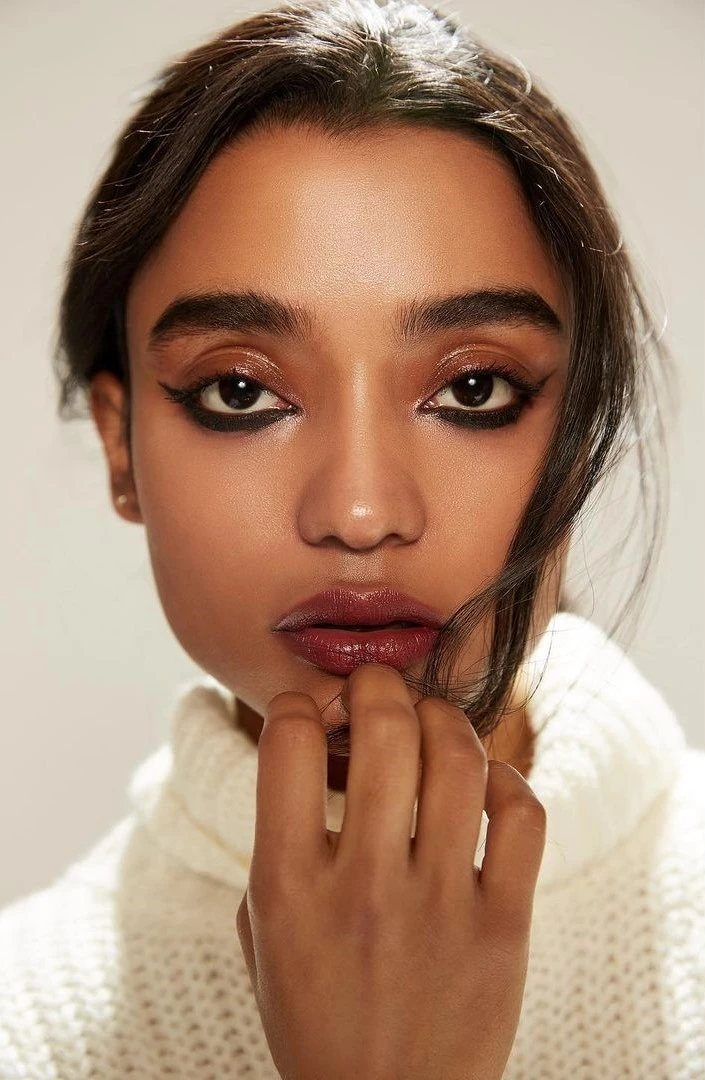 : Close-up of a woman with striking makeup, featuring bold eyeliner and glossy lips.