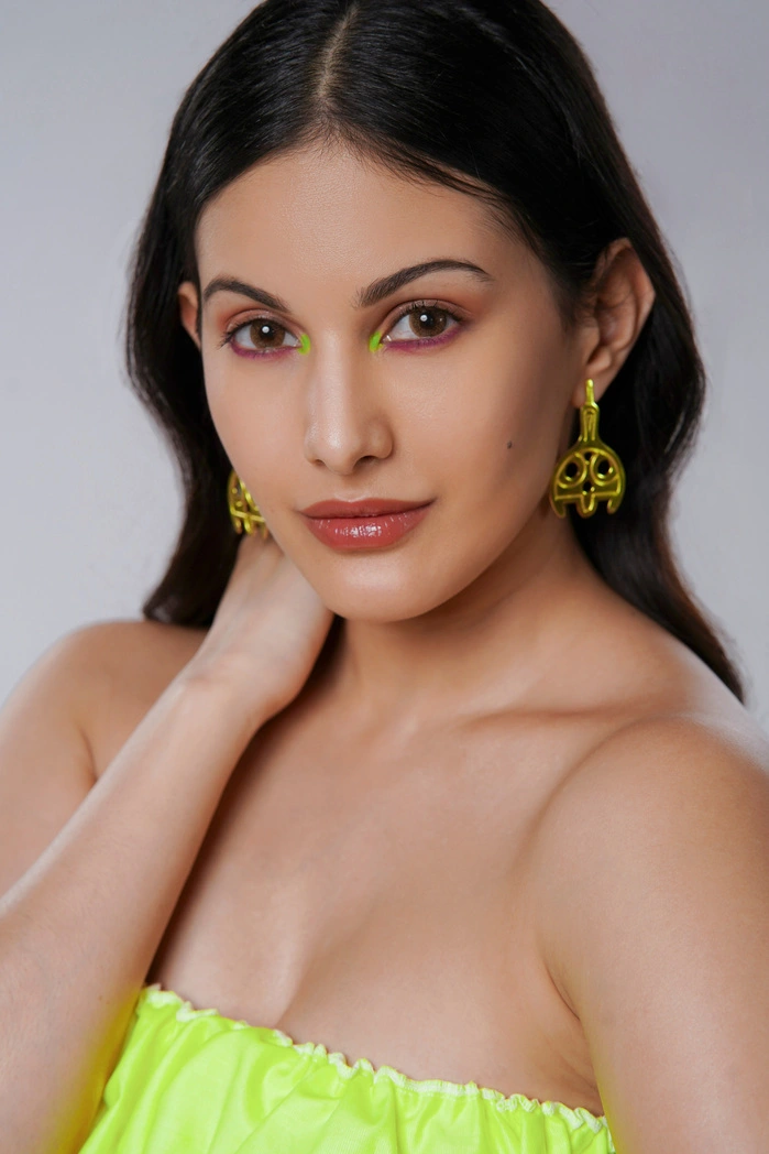 Amyra Dastur posing with a confident expression, wearing vibrant yellow earrings and makeup.