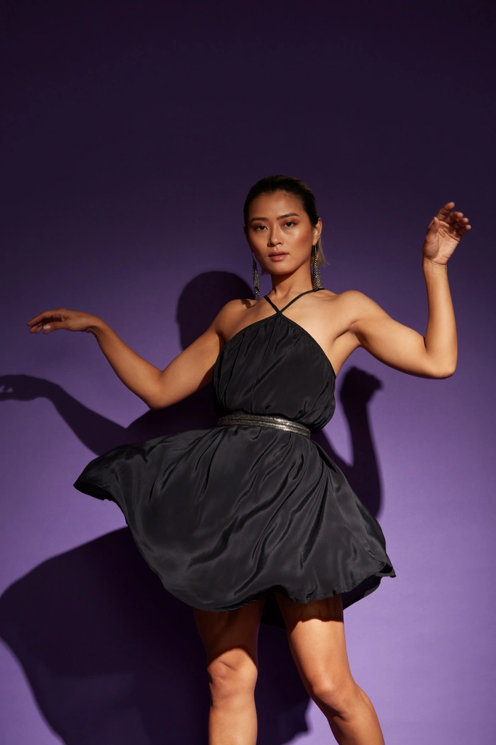 A woman in a black halter dress posing against a purple background.