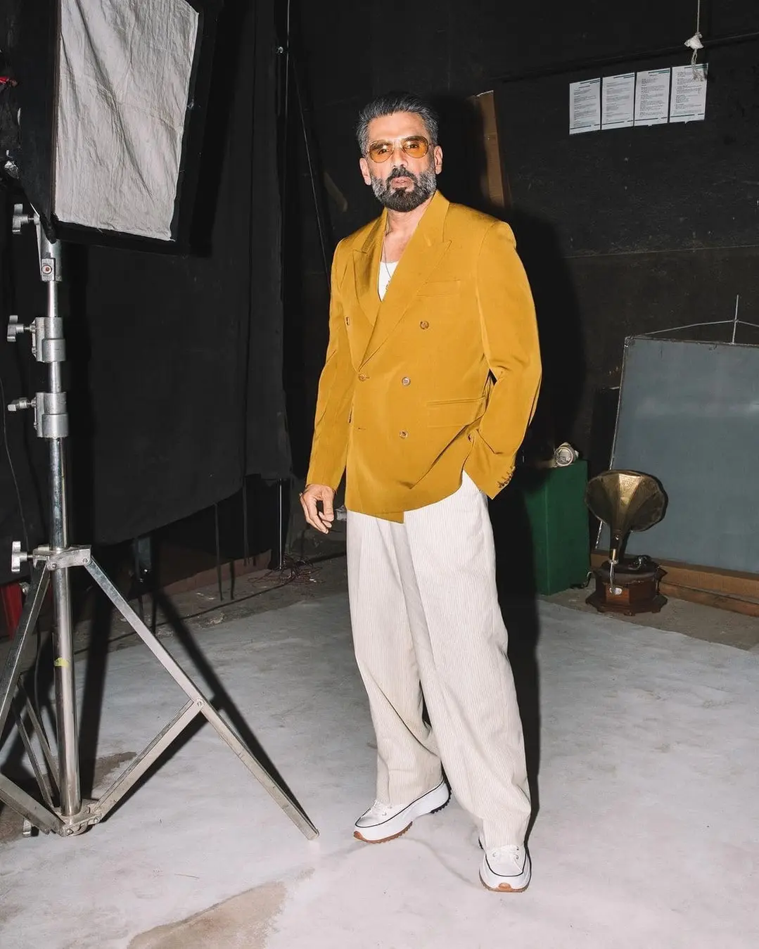 Sunil Shetty posing confidently in a mustard blazer and white trousers.
