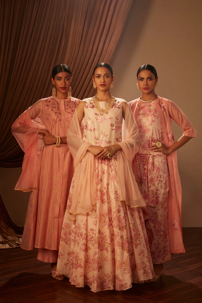 Three women in elegant pink floral outfits, standing together with a soft backdrop.