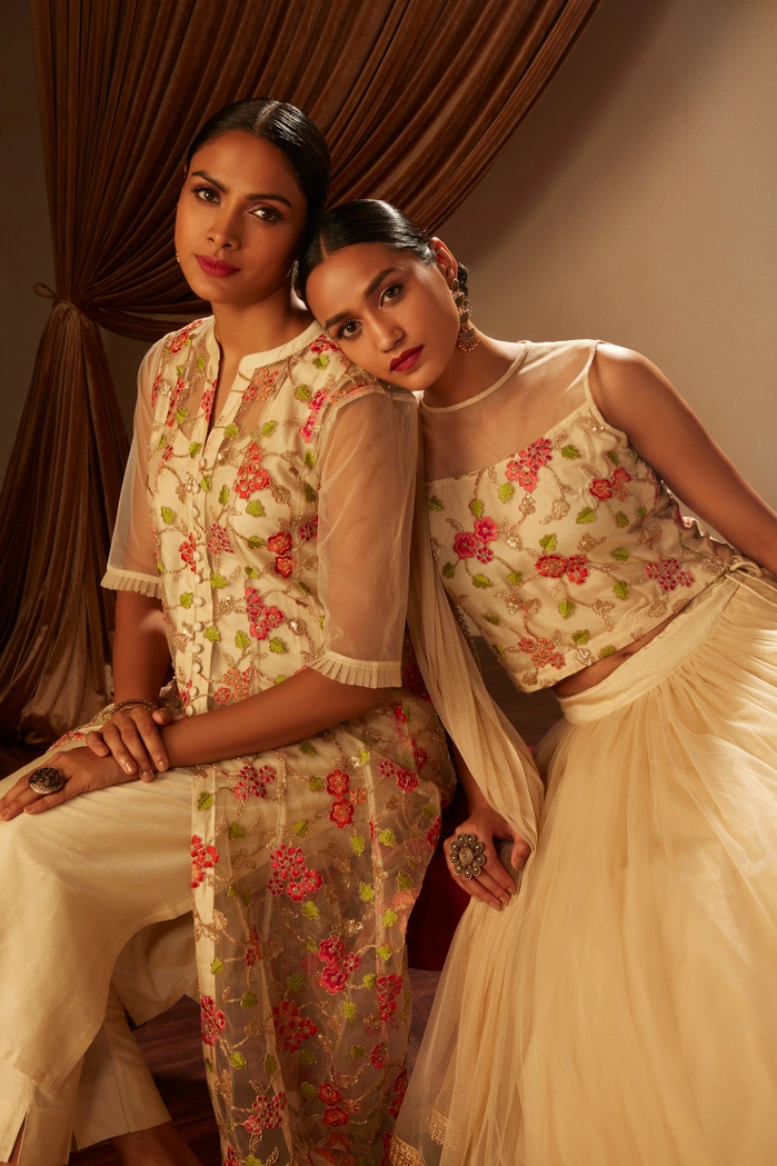 Two women in elegant embroidered outfits, posing closely together.