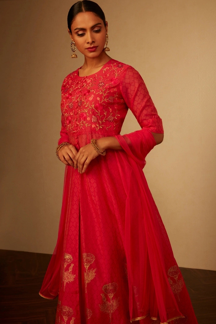A woman in a bright pink embroidered outfit, posing gracefully with a soft expression.