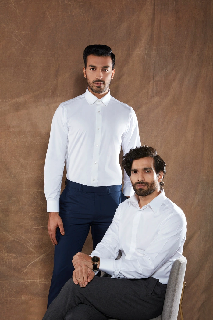 Two men in formal attire, one standing and one seated, against a textured background.